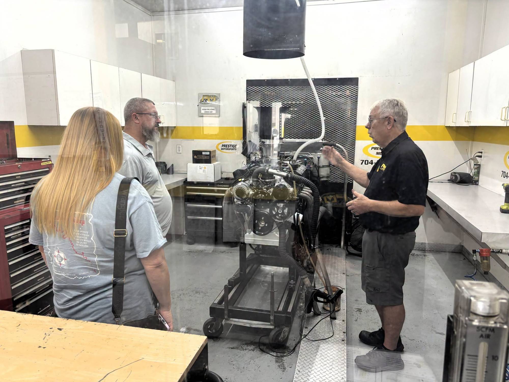 Prestige Motorsports engine builder talking with customers beside an engine in the dyno room
